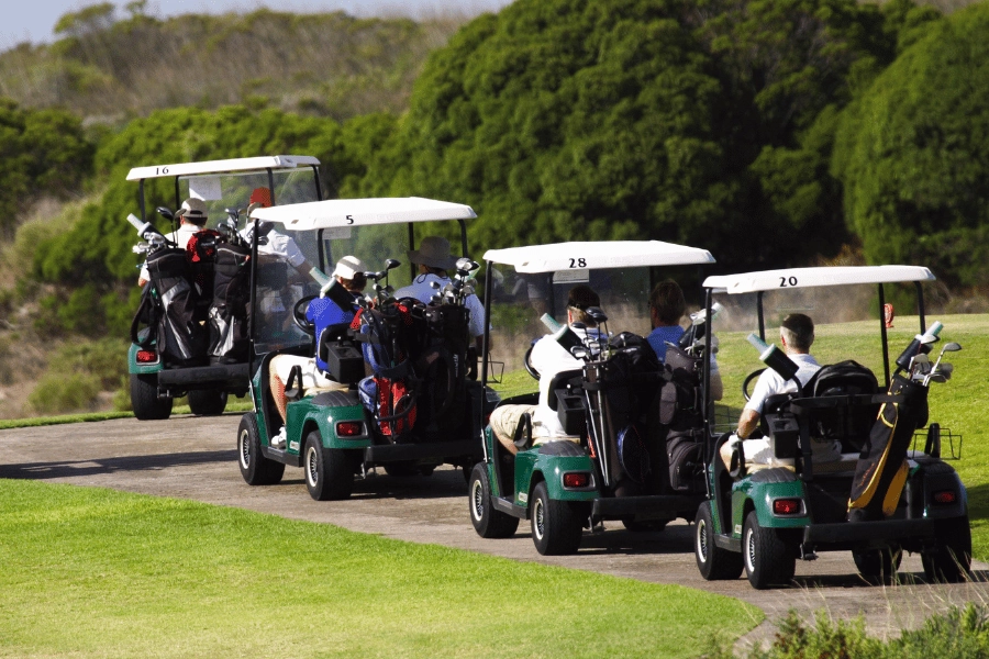 line of four golf carts on a golf course with players and their bags of club